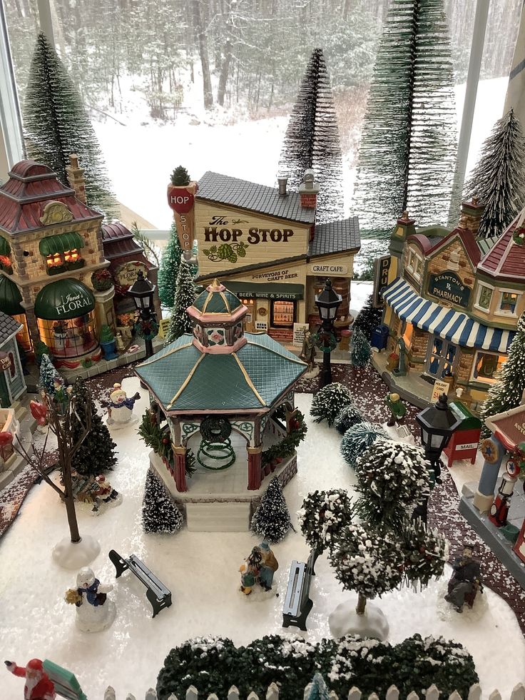This may contain: an assortment of miniature buildings and trees in a window sill with snow on the ground