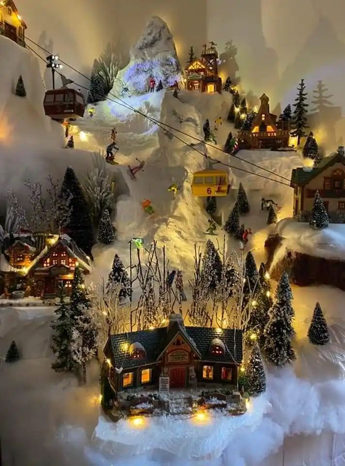 This may contain: a christmas village with lights and trees on the snow covered mountain side is shown in this image