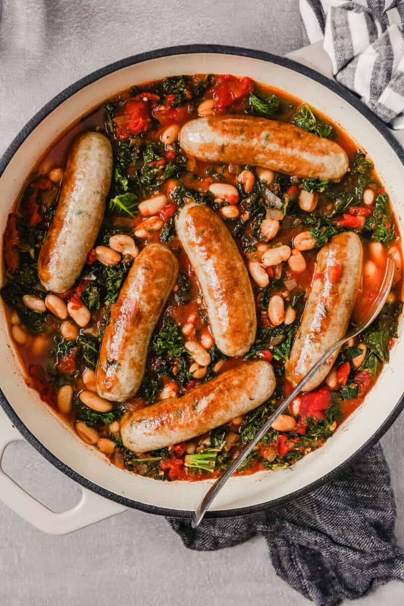 Overhead photograph of a Dutch oven filled with Italian chicken sausages stewed in tomatoes, kale and white beans