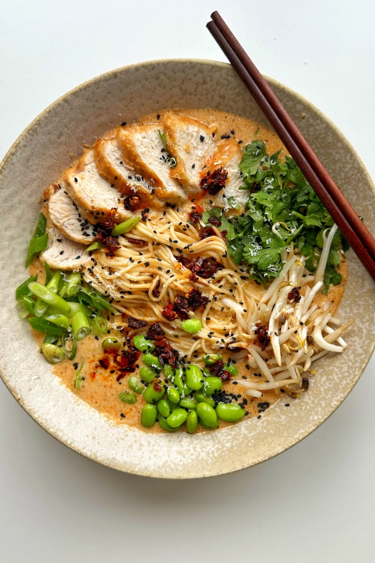 This may contain: a bowl filled with noodles, meat and veggies next to chopsticks