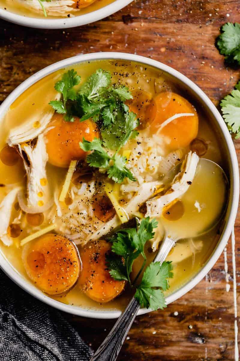 brothy chicken and rice soup with sweet potatoes in a white bowl set on a wood table
