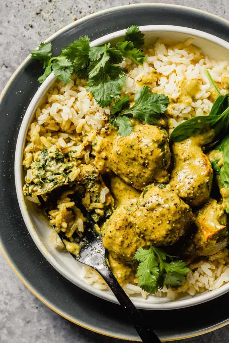 meatballs and a creamy curry sauce served over rice and topped with cilantro in a shallow white bowl